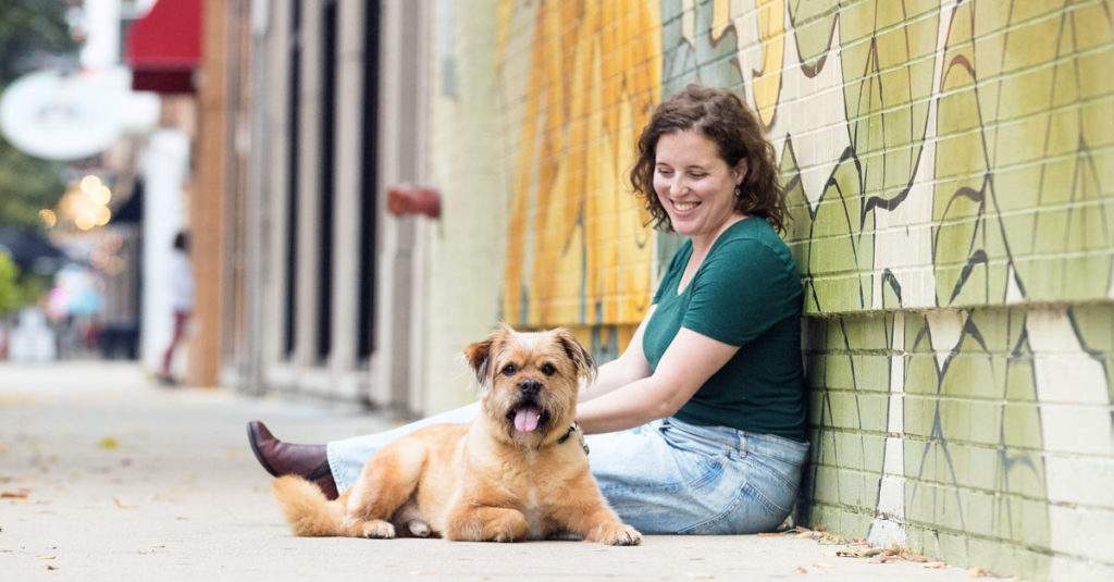 a woman and a dog sitting on a sidewalk